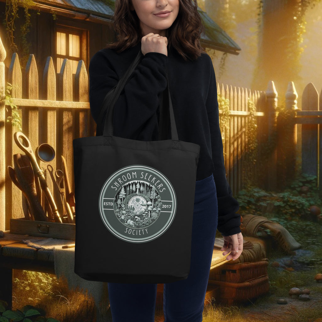 The 'Shroom Seekers Society' black tote over a model's shoulder, showcasing a detailed botanical forest design, merging functionality with a deep appreciation for ecological interconnectedness.