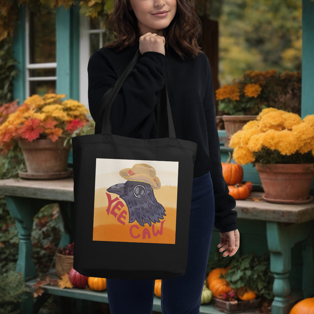 The 'Yee Caw' black tote over a model's shoulder, featuring the unique crow with a straw hat design, merging practicality with a sense of lighthearted fun and creativity.