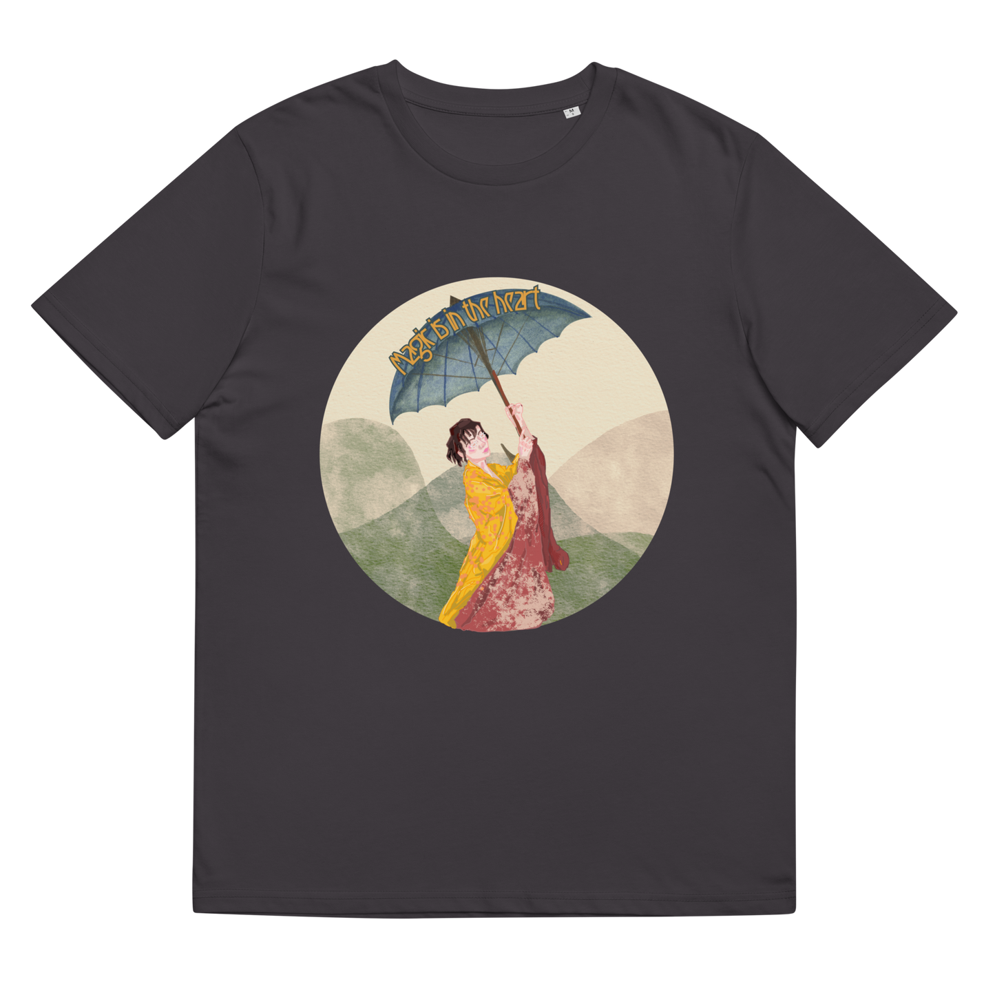 The 'Magic is in the Heart' design on an Anthracite tee, presented in a lay-flat image, features the serene portrayal of traditional attire and landscape, inspiring a connection to cultural roots and personal strength.