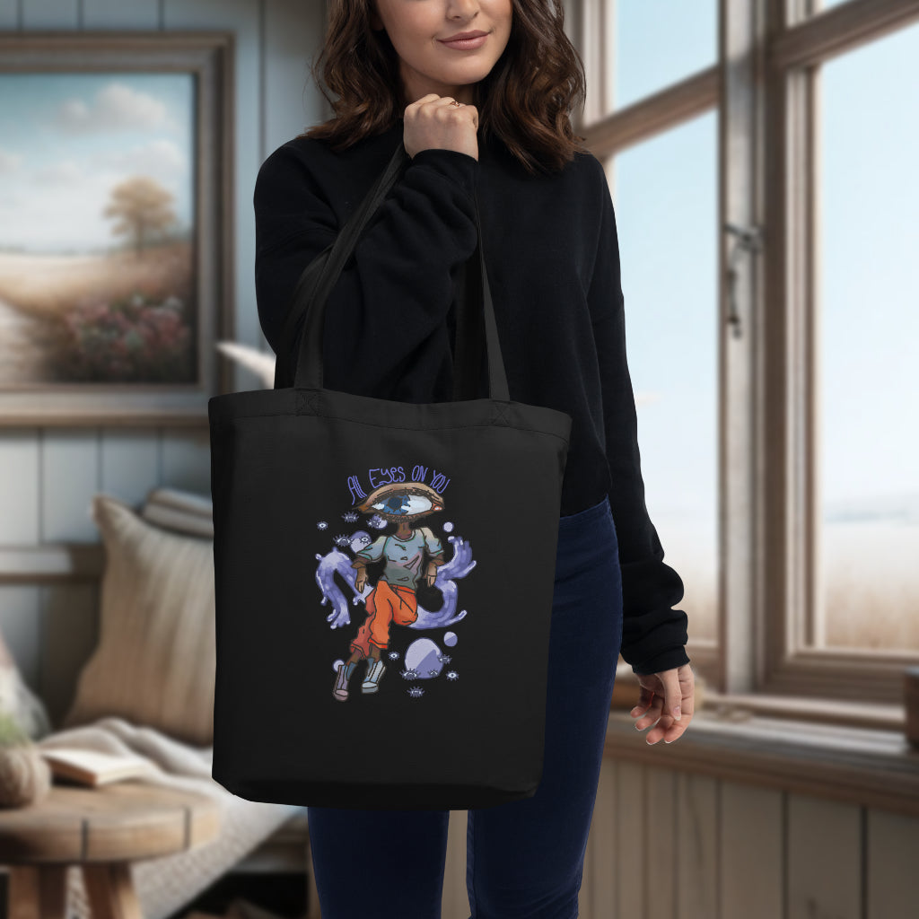 The 'All Eyes On You' black tote slung over a model's shoulder, highlighting the unique and surreal watercolor artwork, serving as a stylish and eco-friendly statement piece for everyday use.