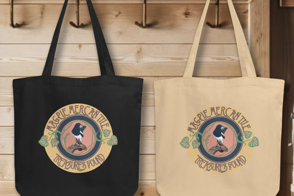 Group display of 'Magpie Mercantile Logo' Totes in black and oyster, hanging on wall hooks, each featuring the elegant watercolor magpie logo, symbolizing the brand's commitment to curating unique and precious finds.