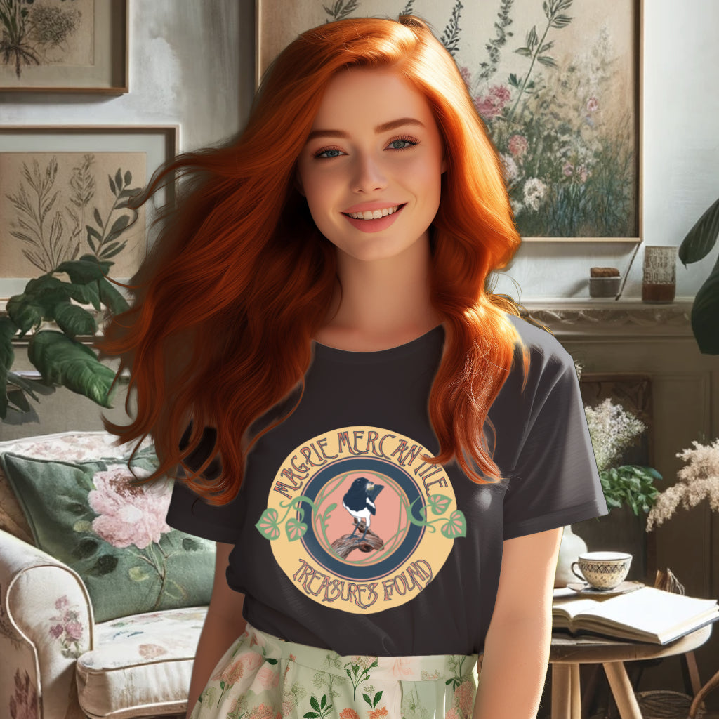 Model wearing the 'Magpie Mercantile Logo' T-Shirt in Anthracite, showcasing a watercolor magpie with a gold ring and an Art Nouveau botanical frame, symbolizing the brand's ethos of unique and precious finds.