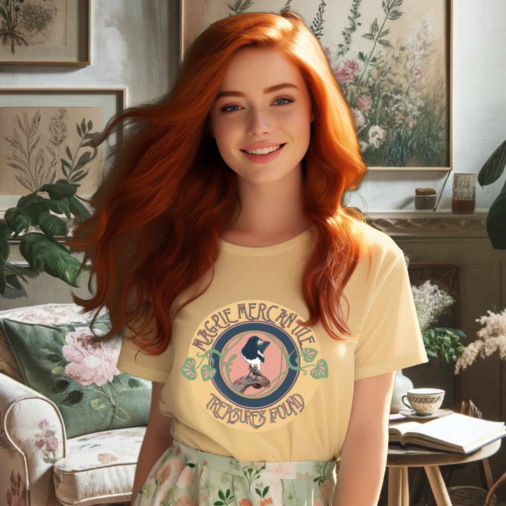 Model wearing the 'Magpie Mercantile Logo' T-Shirt in Butter, showcasing a watercolor magpie with a gold ring and an Art Nouveau botanical frame, symbolizing the brand's ethos of unique and precious finds.