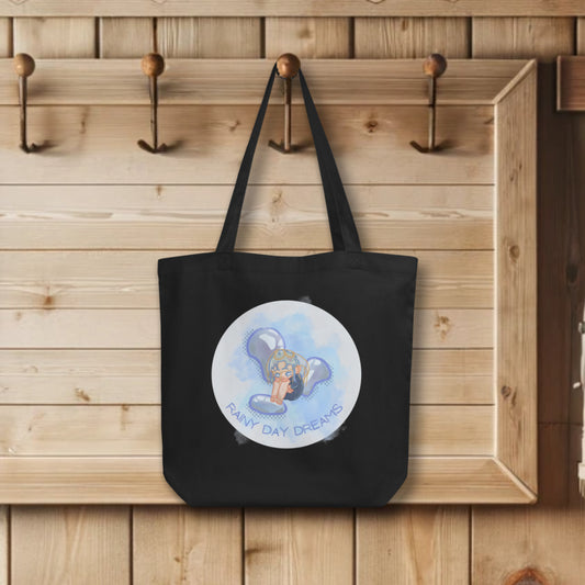 'Rainy Day Dreams' Totes in black, hanging on wall hook, featuring the tender watercolor design of a teary Chibi character, symbolizing the poignant emotions of rainy days and the power of dreams.