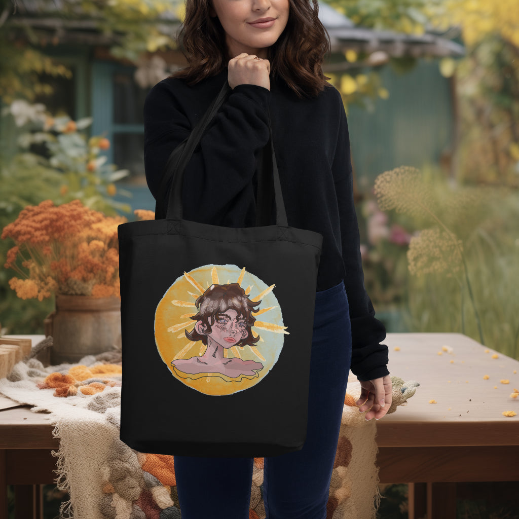 Model carrying the 'Sunshine Girl' Tote in black, accentuating the pensive girl's watercolor portrait set against a sun, a perfect blend of functionality and thought-provoking artistry.