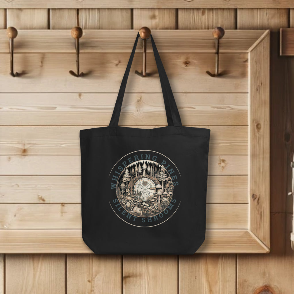 'Whispering Pines, Silent Shrooms' Tote Bags in black, displayed on hooks, featuring a serene forest ecosystem with mushrooms and pines in a circular design, symbolizing nature's quiet symphony.